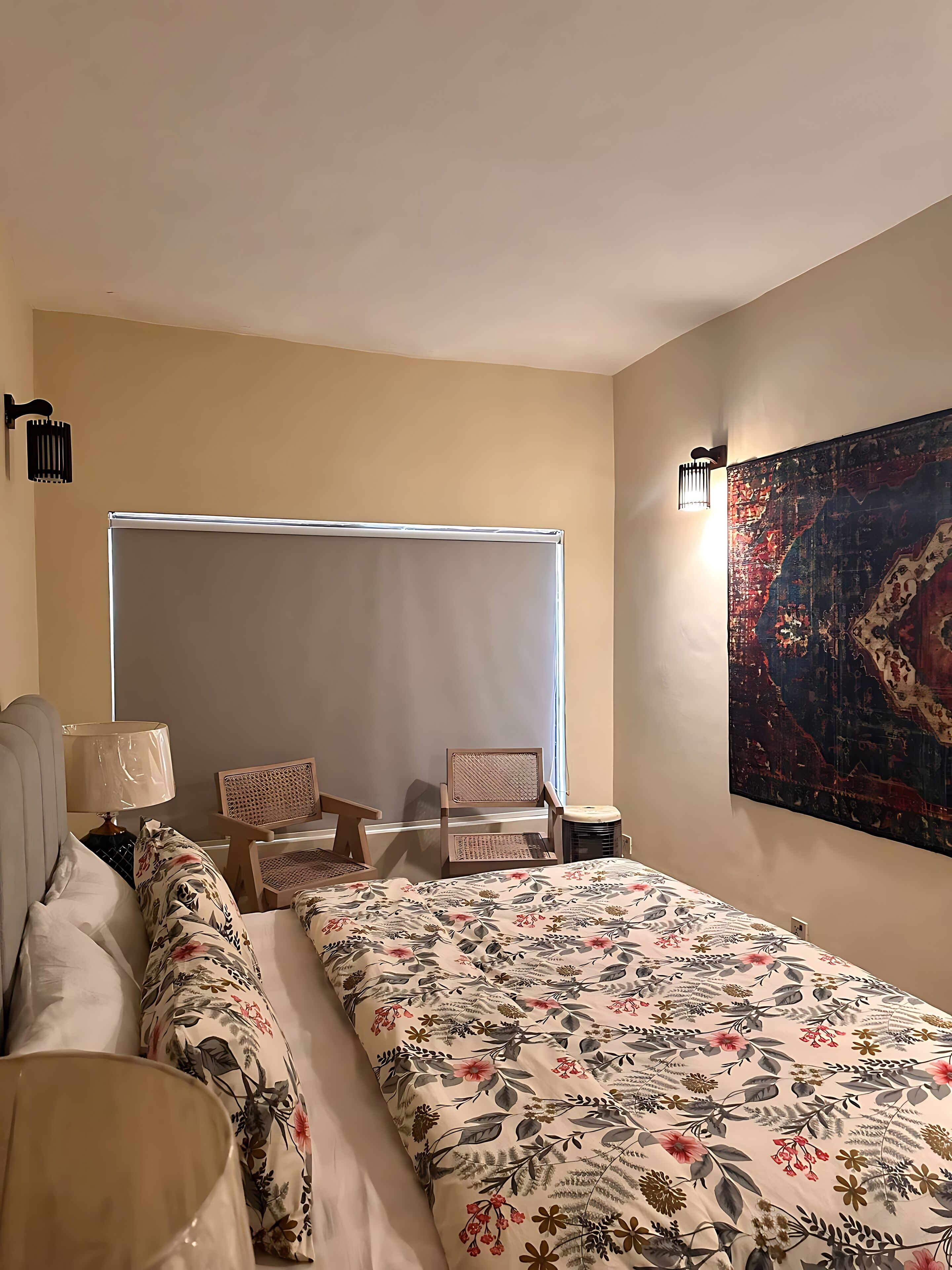 A hotel room with a large bed, a chair, a small table, and a wall-mounted lamp.