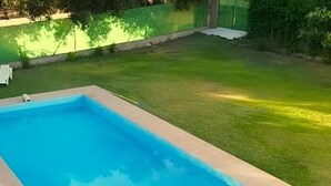 A rectangular swimming pool with a light blue interior, surrounded by a concrete deck and a grassy lawn.