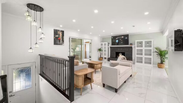 A modern living room with a fireplace, white sofas, a TV mounted on the wall, and a staircase with a railing.
