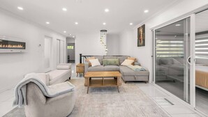 A modern living room with a fireplace, a sofa, a coffee table, and a sliding glass door leading to a bedroom.