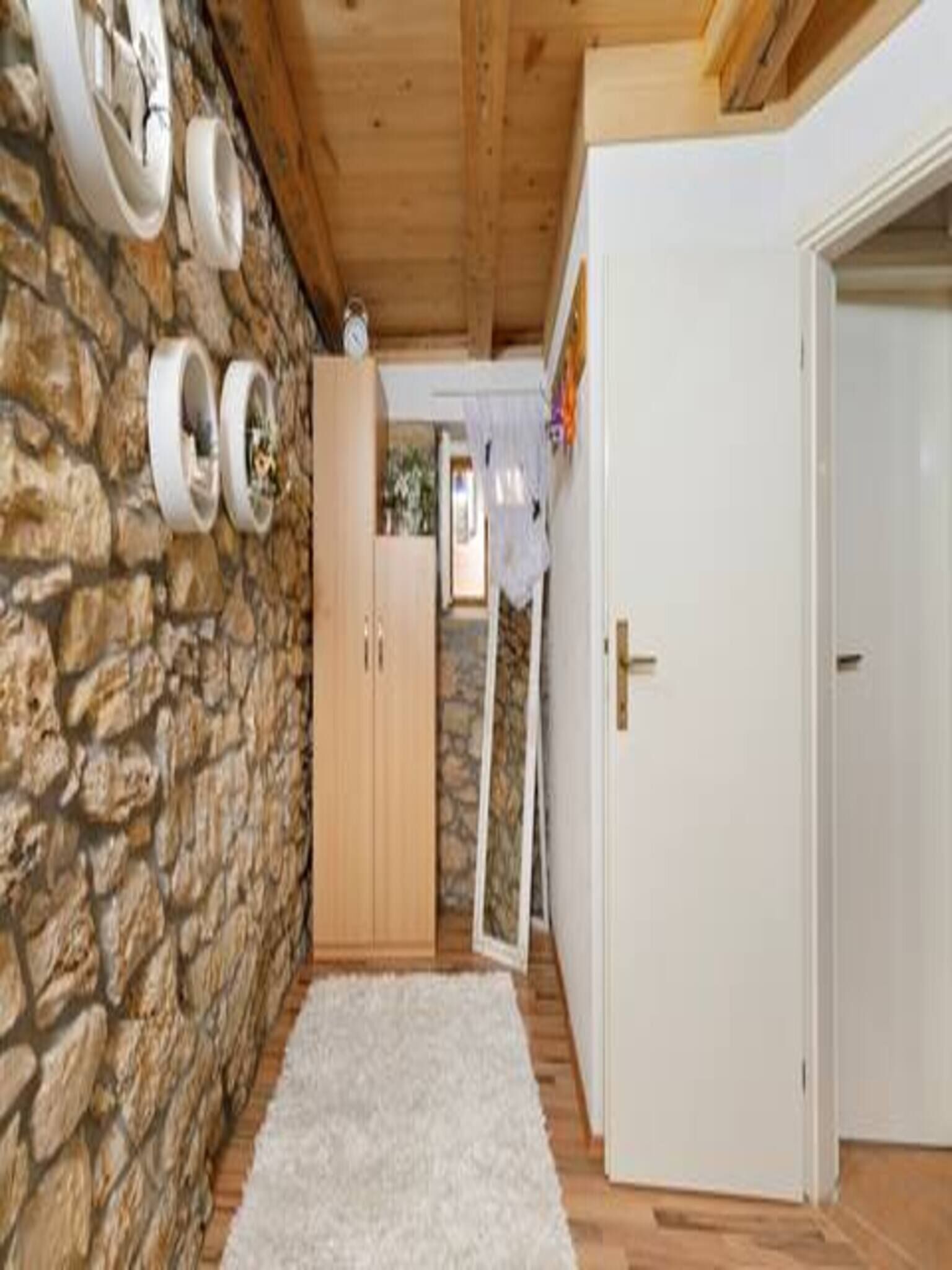 Un corridoio con una parete in pietra, una porta in legno e un tappeto bianco.