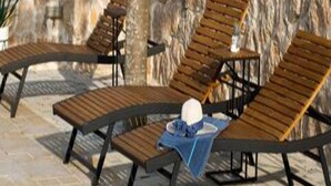 Een stenen muur met een houten terras en vier loungestoelen.