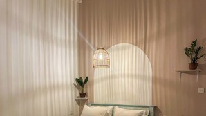 Une chambre à coucher comprenant un lit, une table de chevet, un luminaire suspendu, une plante en pot et une étagère fixée au mur.