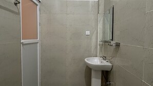 Une petite salle de bain étroite, avec un lavabo blanc, un miroir et une cabine de douche.