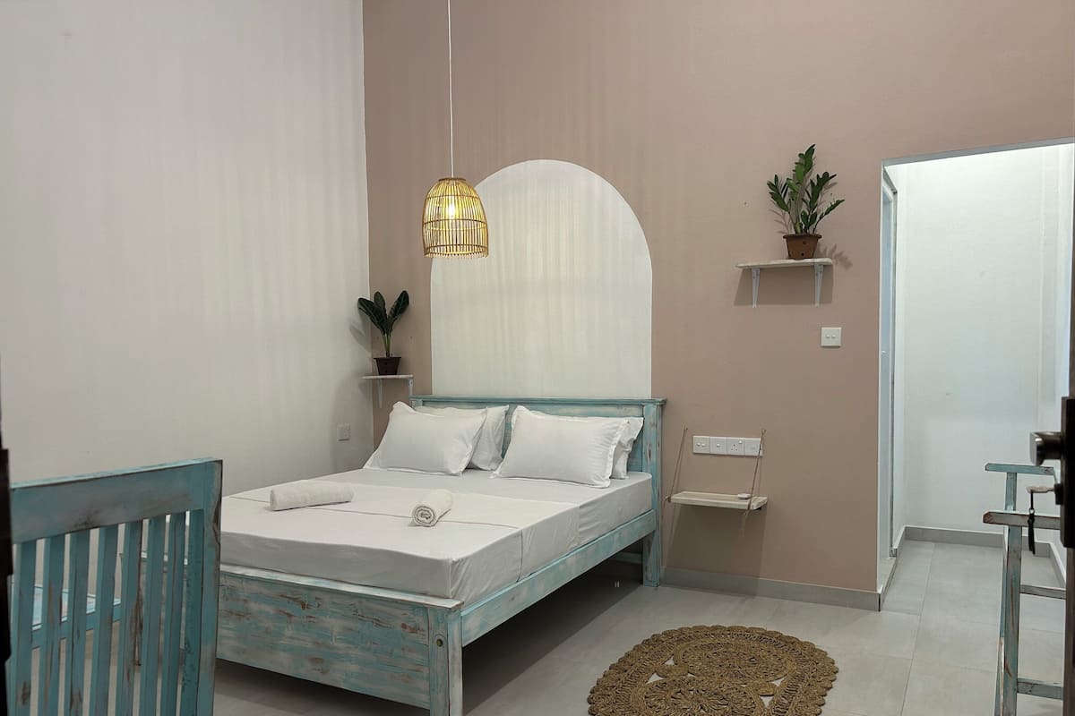 Une chambre à coucher avec un lit, une table de chevet, une lampe suspendue, des plantes en pot et une porte.