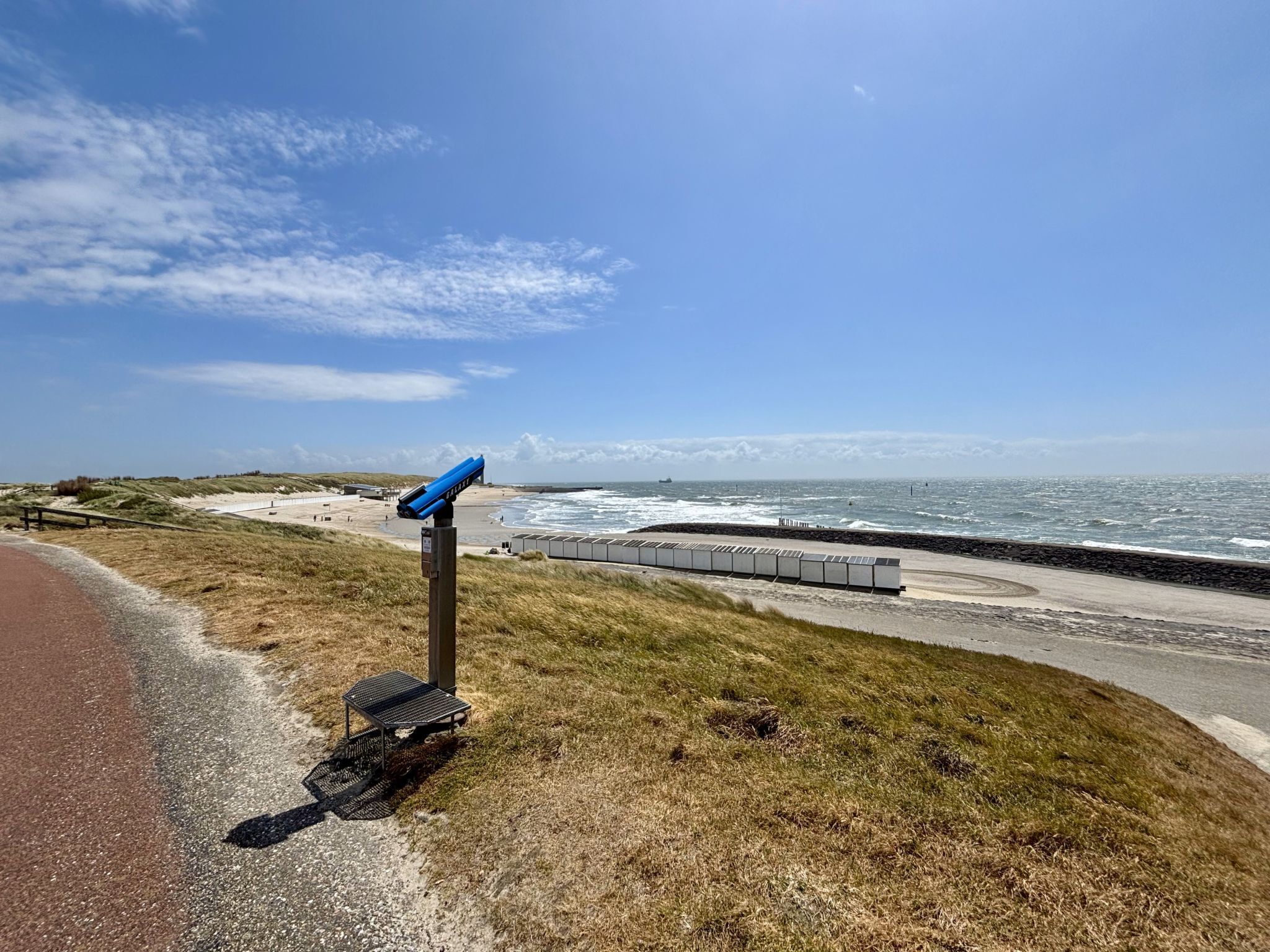 Ein Küstenblick mit Teleskop, einem gepflasterten Weg und einem Strand im Hintergrund.