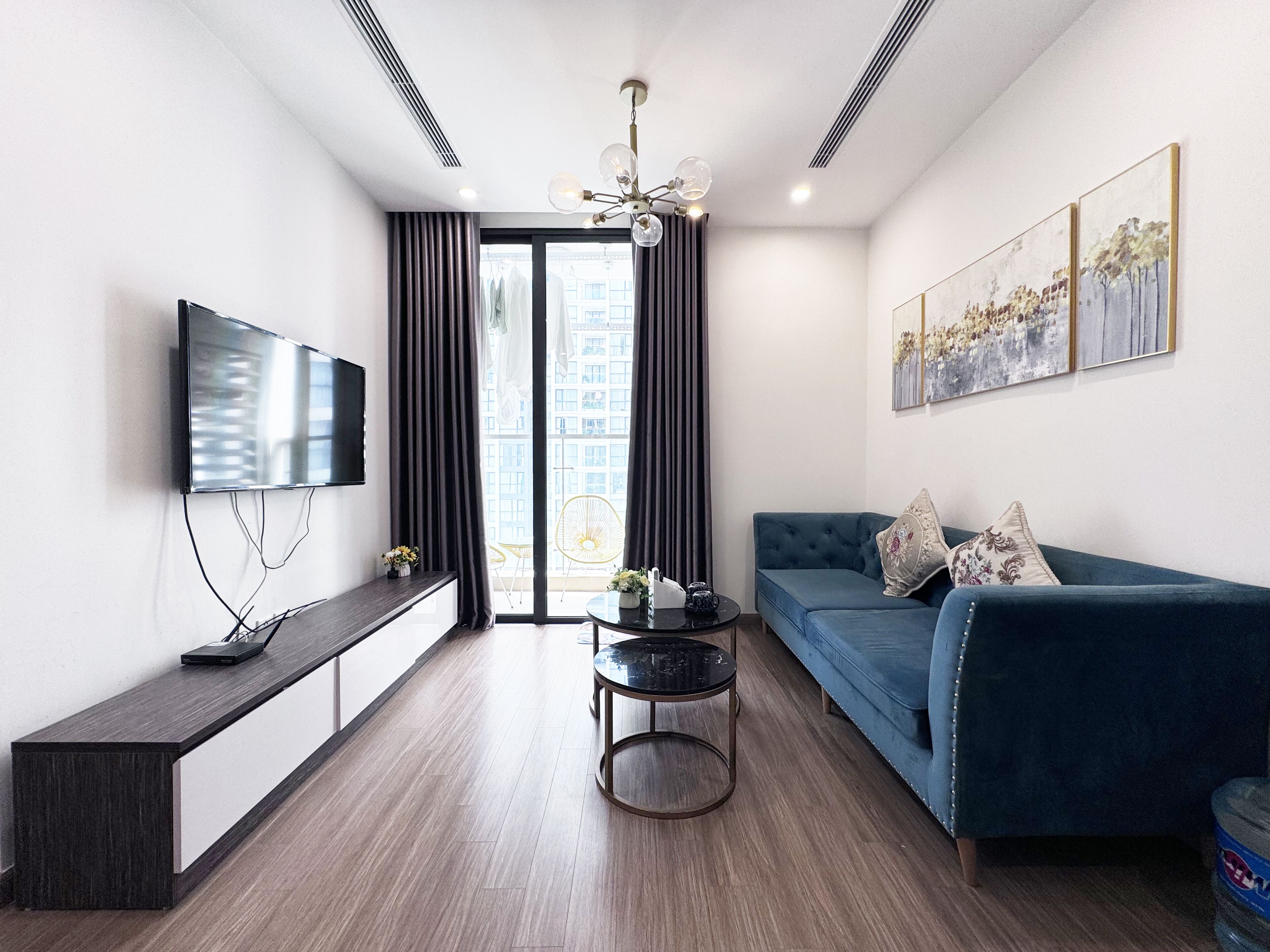 Een moderne woonkamer met een flatscreen televisie, een blauwe bank, een ronde salontafel en een bankje.