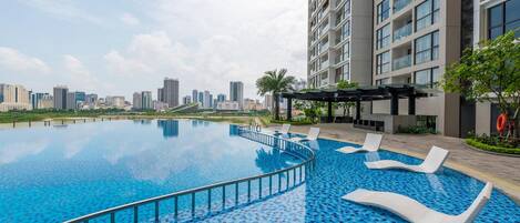 A modern hotel with a large infinity pool, lounge chairs, and a city skyline view.