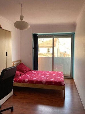 Ein Schlafzimmer mit Bett, Sessel, Deckenventilator und Fenster mit Blick auf Gebäude.