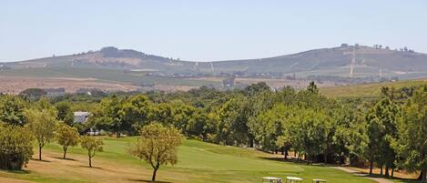 A golf course with a clear path, trees, and distant hills.
