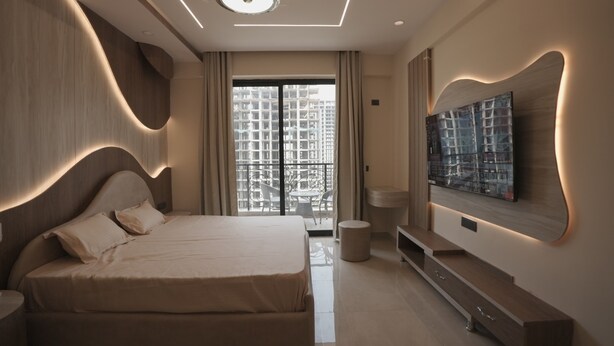 A modern bedroom with a large bed, a flat-screen TV mounted on the wall, and a balcony with a city view. - Villa Vistosa Omaxe Hazratganj (Lucknow)