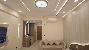 A modern hotel room with a curved sofa, a TV, and a built-in circular light fixture. - Villa Vistosa Omaxe Hazratganj (Lucknow)