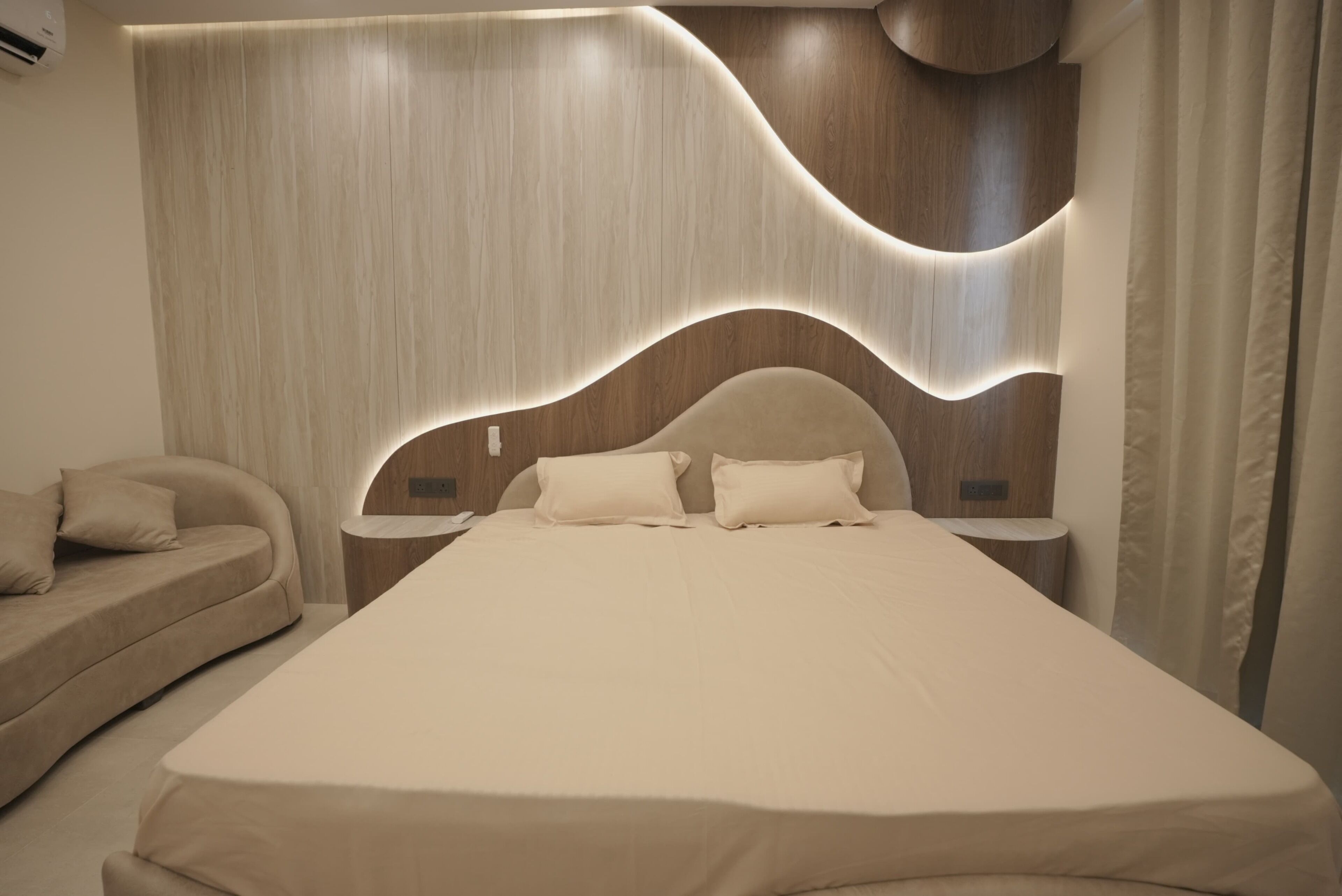 A modern bedroom with a curved headboard, a large bed, a bedside table, and a sofa.