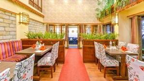 A restaurant with wooden tables and benches, a red carpet, and green plants. - The Oriental (Gangtok)
