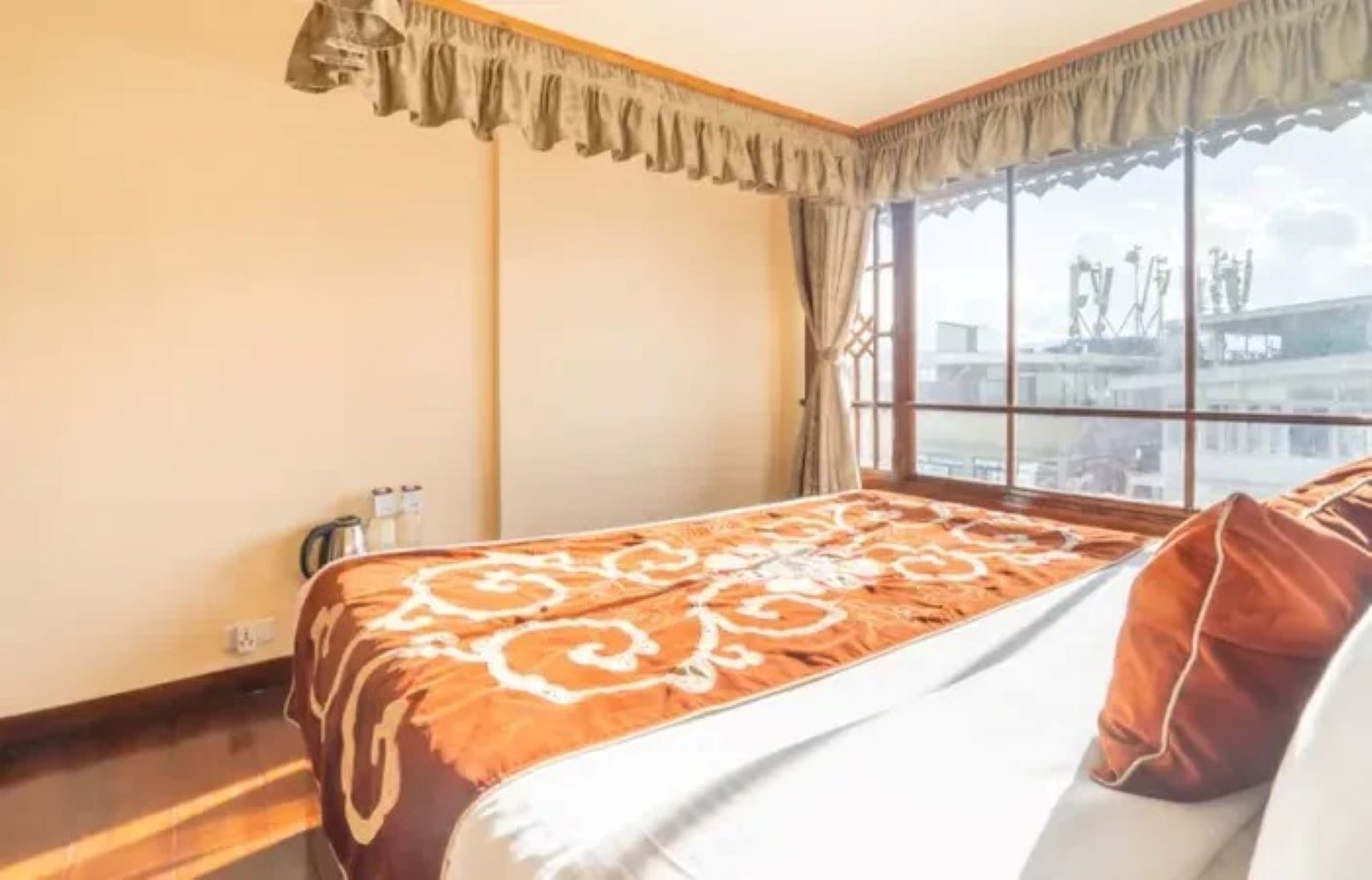 A hotel room with a large window, a bed with a patterned bedspread, and a wooden floor.