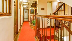 A hallway with a red carpet, wooden railings, and a staircase with a metal railing. - The Oriental (Gangtok)