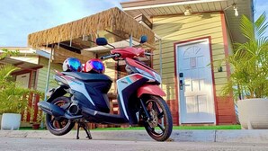 A Yamaha scooter parked in front of a house with a thatched roof and a white door.
