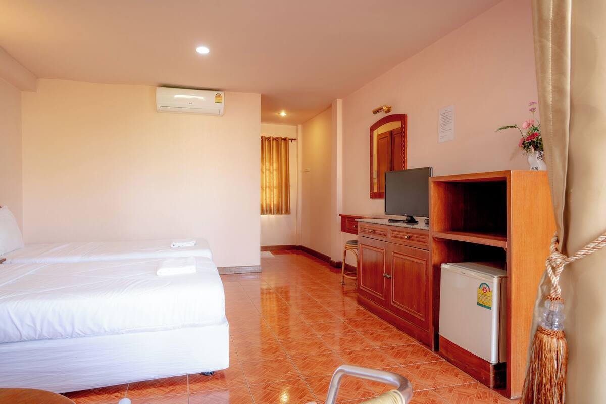 A hotel room with two beds, a TV, a refrigerator, and a bathroom with a shower curtain.