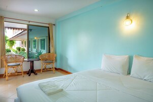 Un dormitorio con una cama, dos sillas, una mesa y un ventanal con cortinas.