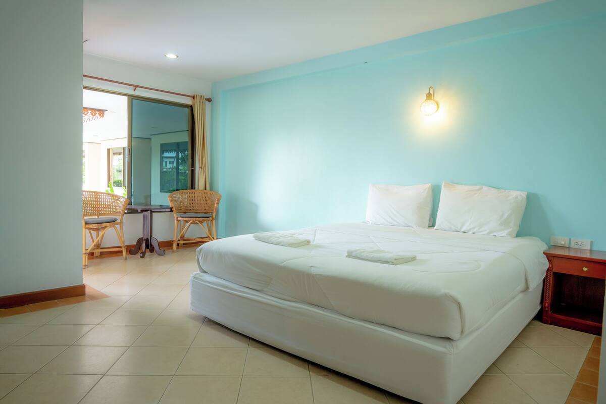 A hotel room with a large bed, a small table with chairs, and a wall-mounted light fixture.