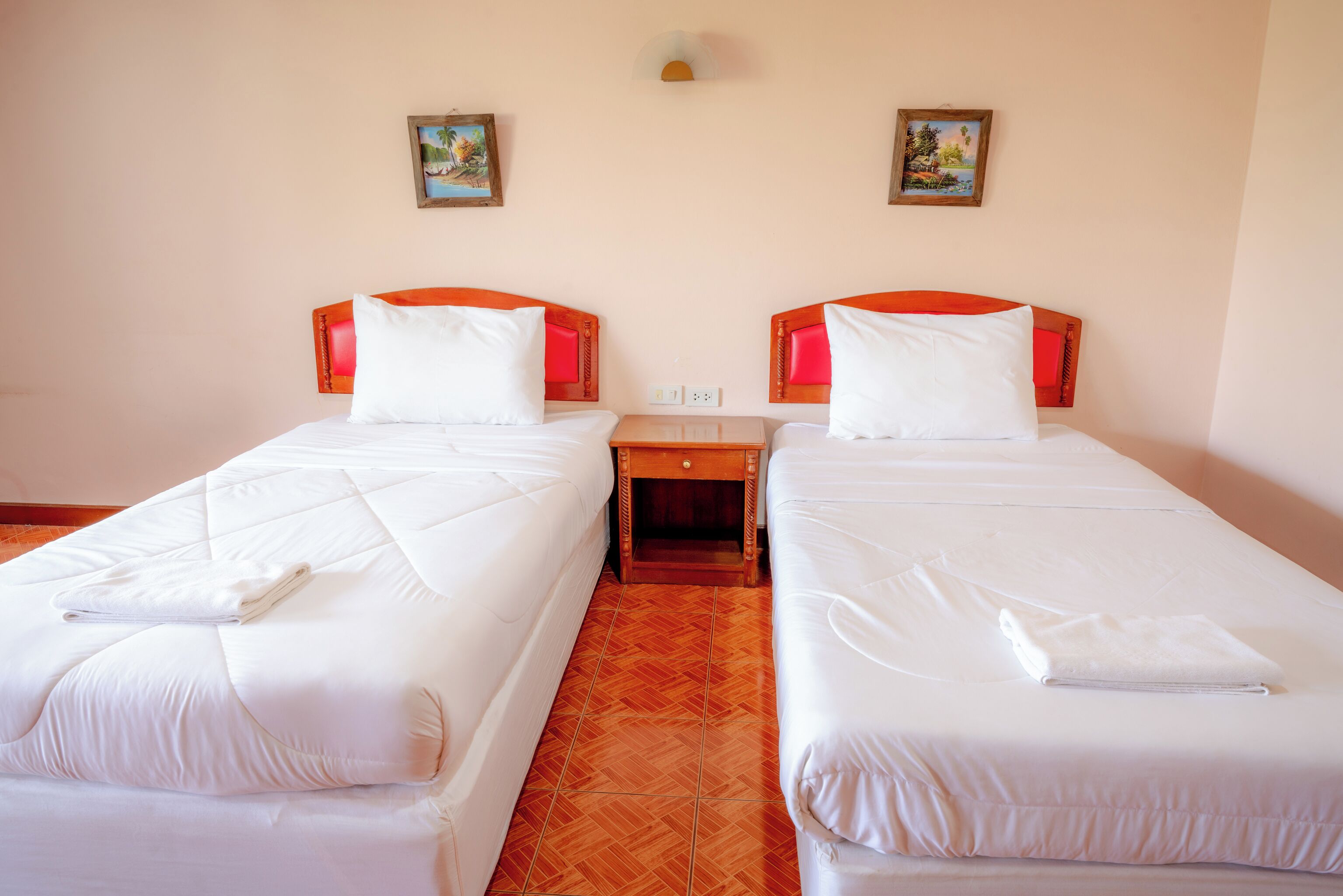 A hotel room with two single beds, each with a red headboard, white bedding, and a small wooden nightstand between them.