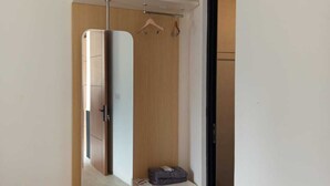 Une chambre à coucher de taille réduite, comprenant un lit, une petite table de chevet, un porte-vêtements suspendu et une armoire intégrée.