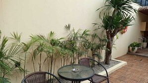 Une terrasse extérieure avec une table ronde et des chaises en osier, entourée de plantes en pot et d’un palmier.