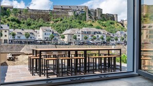 Terraço com mesas ao ar livre, com vista para uma cidade histórica, com edifícios e um castelo numa colina.