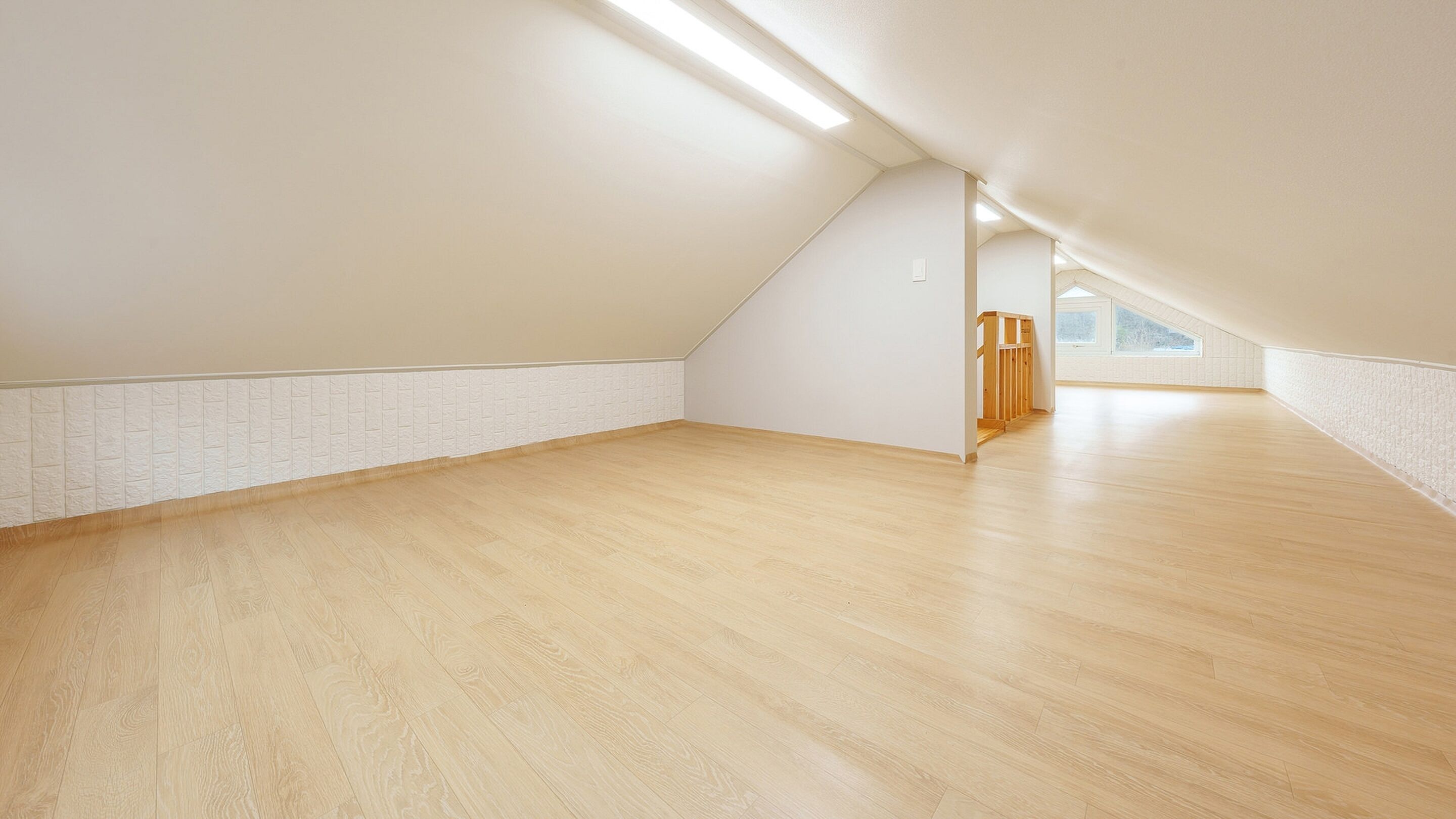 A spacious attic room with wooden flooring, white walls, and a sloped ceiling.