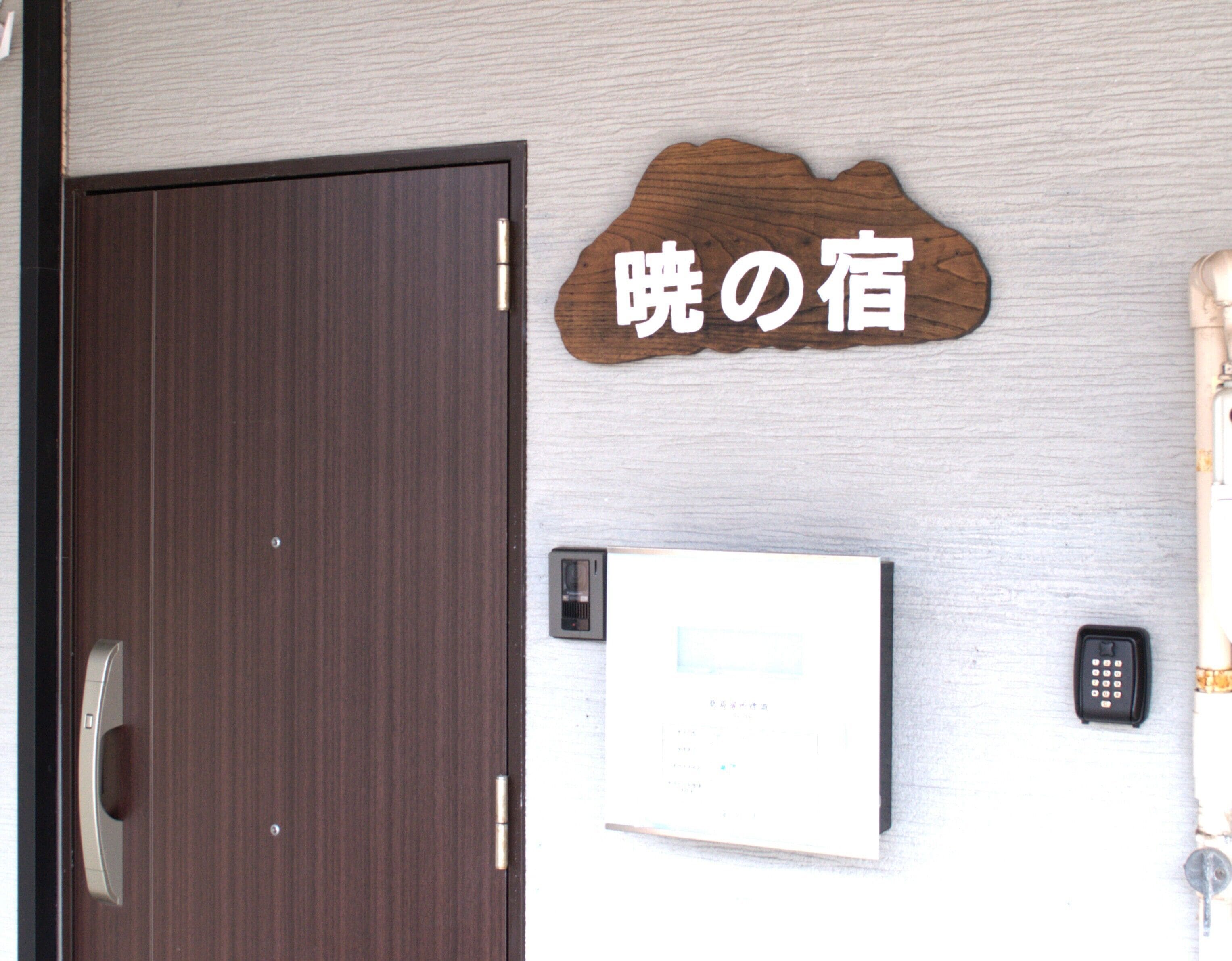 A wooden sign with Japanese characters, a door, a wall-mounted intercom, and a key.