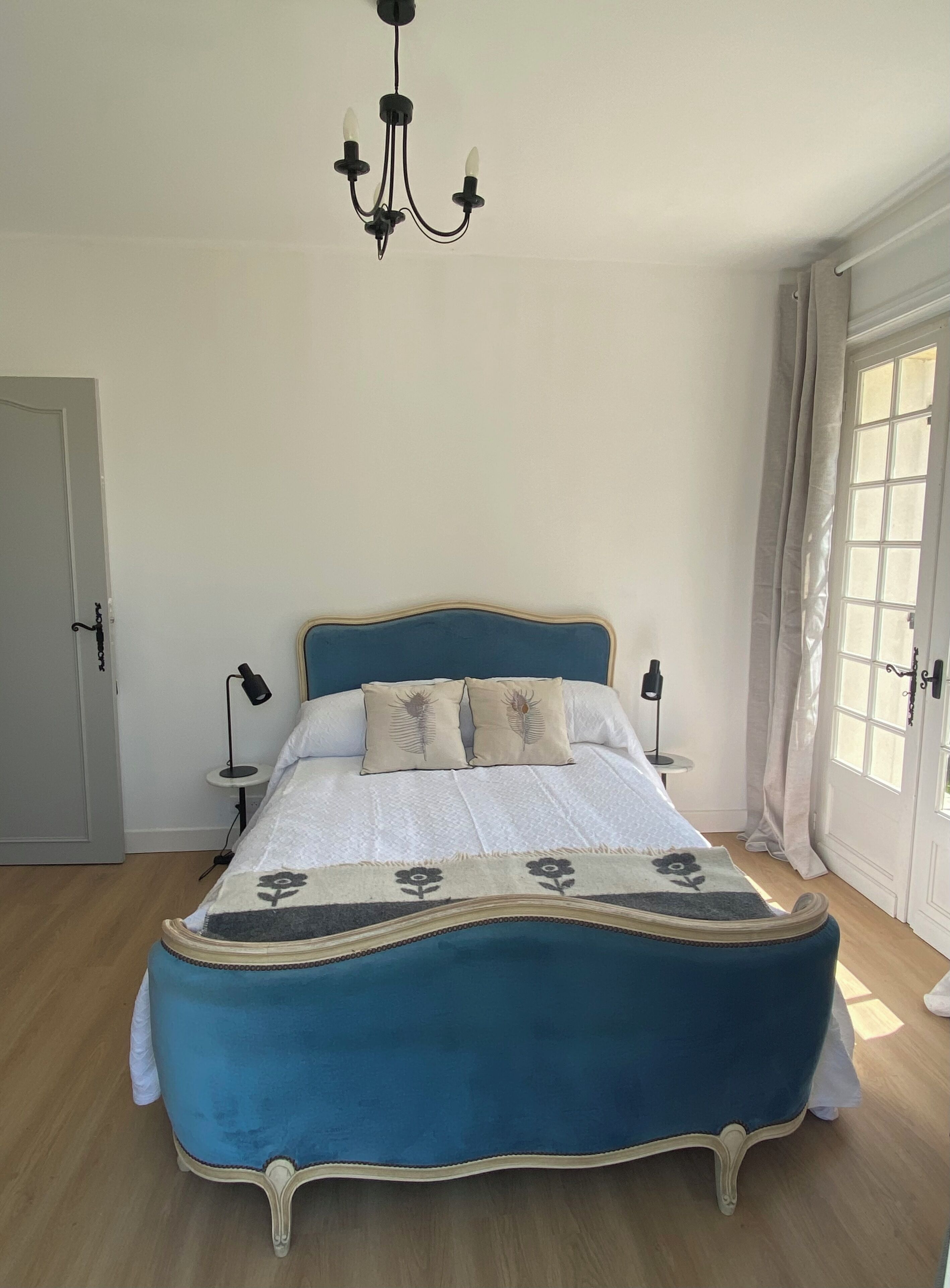 Ein Schlafzimmer mit einem großen Bett, einer Chandelüster, einem Fenster mit Vorhängen und einer Tür.