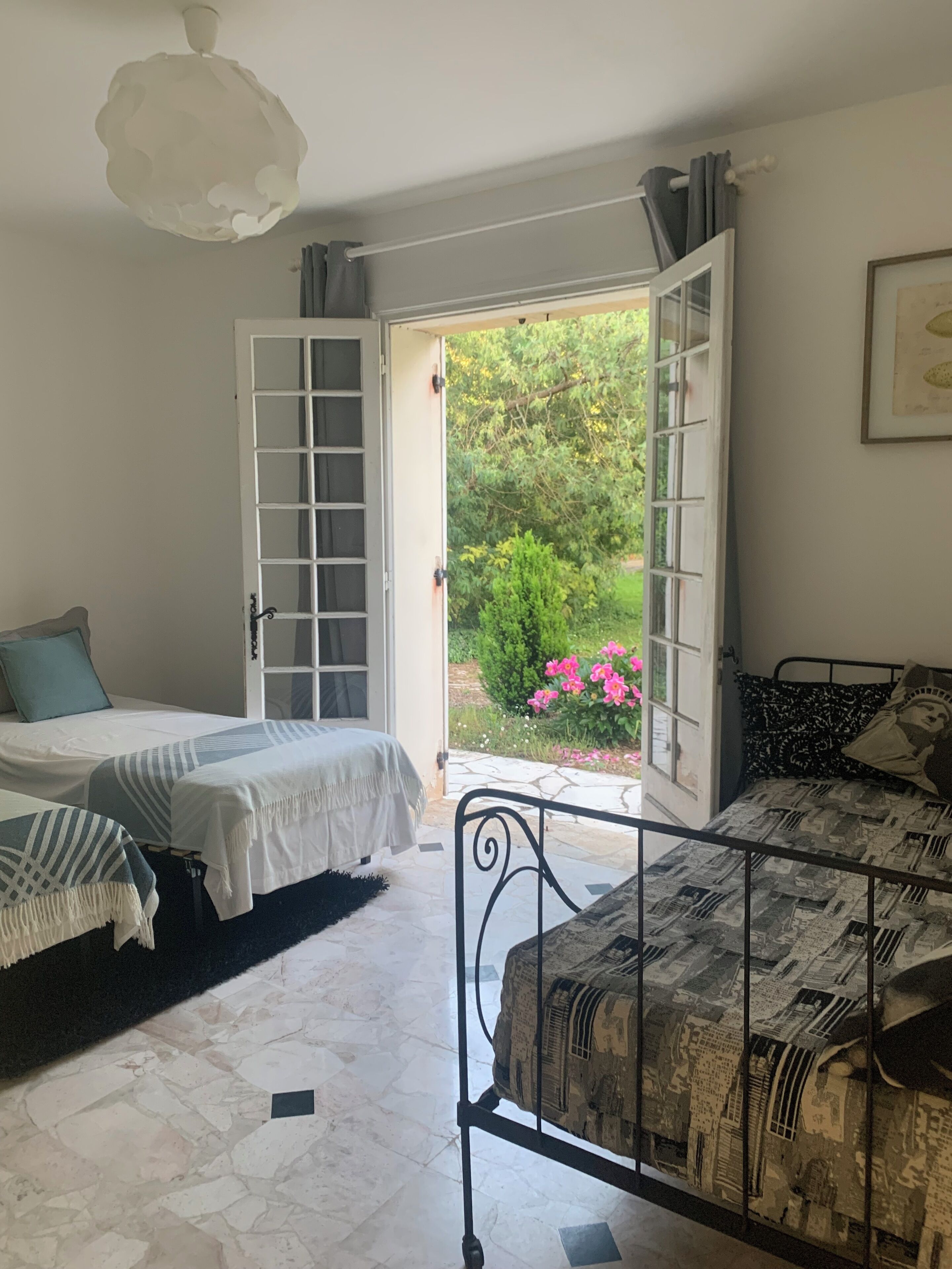 A bedroom with two beds, a large window, and a view of greenery outside.