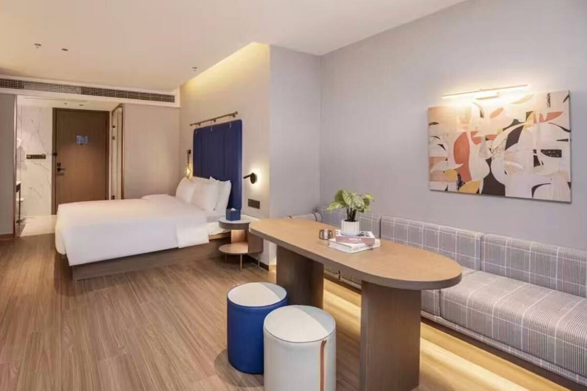 Una habitación de hotel moderna con una cama, un sofá, una mesita y una obra de arte en la pared.