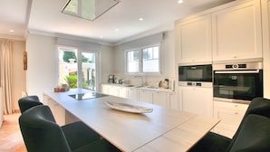 Une cuisine moderne avec des armoires blanches, un grand îlot central et des appareils électroménagers intégrés, notamment un four et un micro-ondes de la marque Bosch.