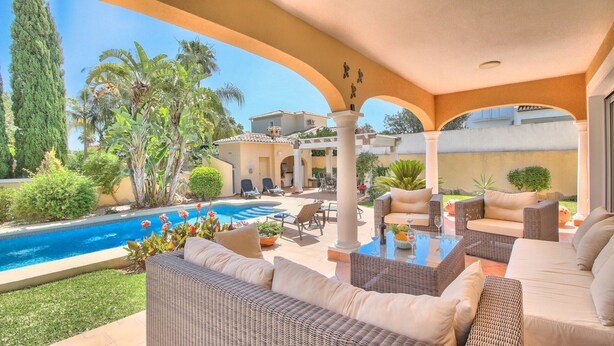 Un espace aménagé au bord de la piscine, avec des meubles en osier, une piscine et une végétation luxuriante tout autour.