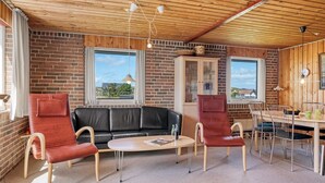 A cozy room with a brick wall, a black leather sofa, two red chairs, a round table, and a dining area with chairs and a table. - "Ava" - 350m from the sea by Interhome (Harboøre)