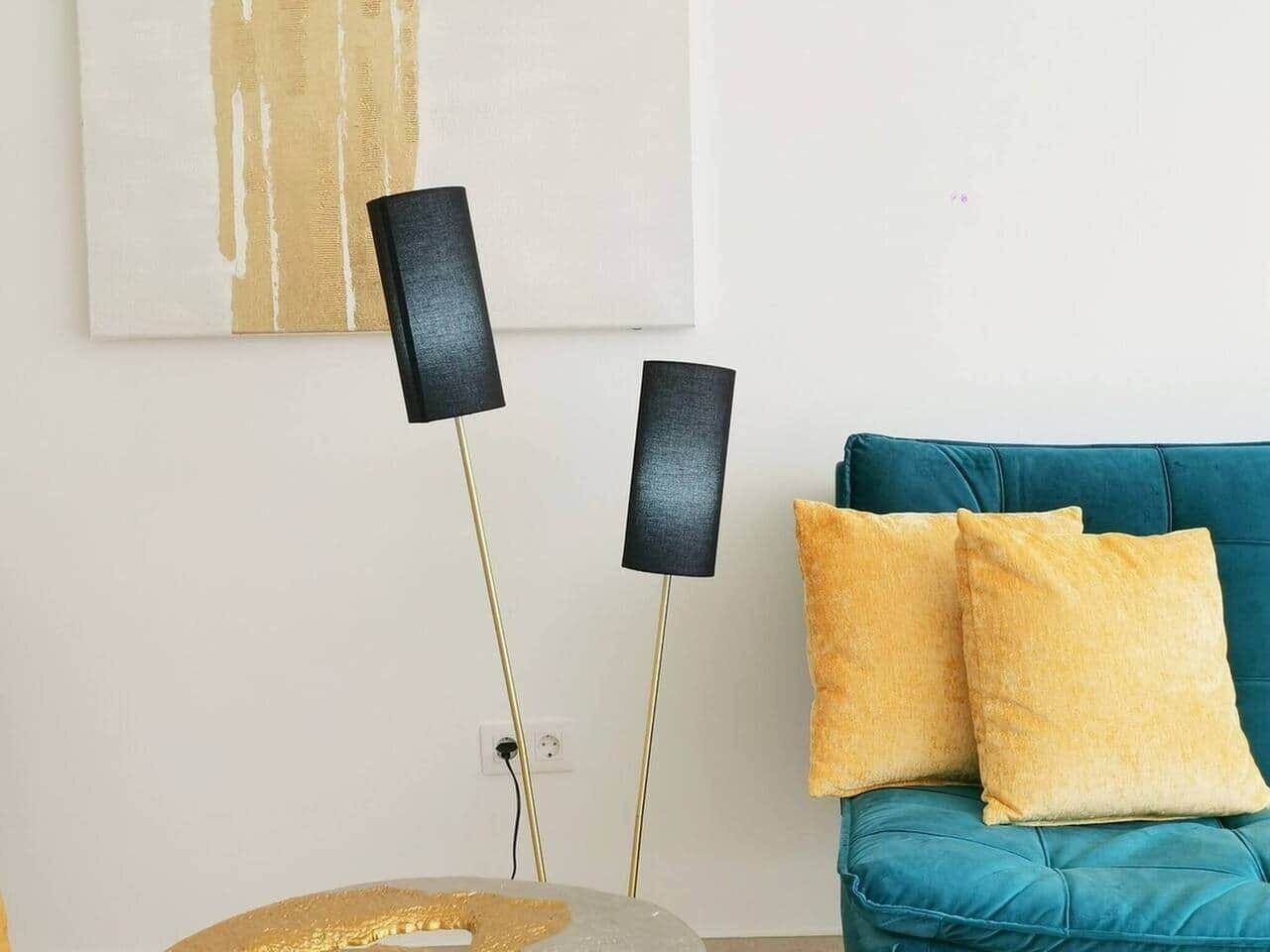 A room with a teal sofa, two black floor lamps, and a gold-framed mirror.