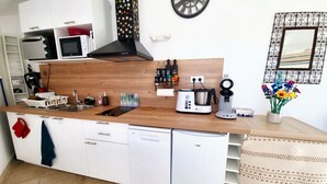 A compact kitchen with a wooden countertop, white cabinets, a built-in dishwasher, a coffee maker, and a wall clock. - Cosy, fully-equipped Tiny House - private garden (Castanet-Tolosan)