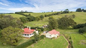 Una propiedad rural con dos edificios principales, uno de techo rojo y otro de techo blanco, rodeada de exuberante vegetación y colinas onduladas.