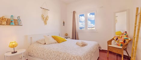 A bedroom with a bed, bedside table, lamp, wall decor, window, and a chair.