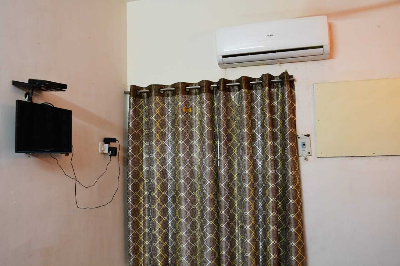 A room with a TV mounted on the wall, an air conditioner, and a patterned curtain.