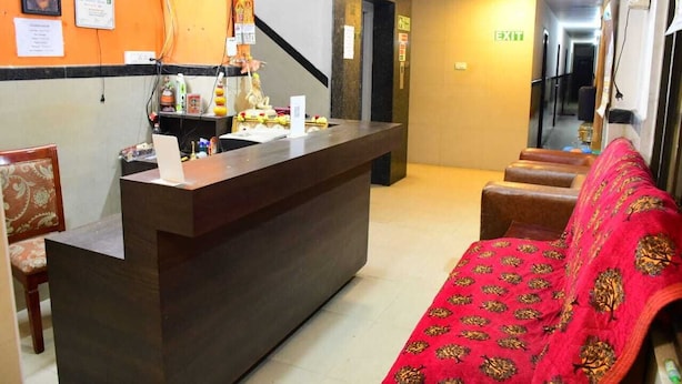 A reception area with a dark reception desk, a red patterned sofa, and a staircase leading to an upper level. - Sai Nalam Guest Inn (Chennai)