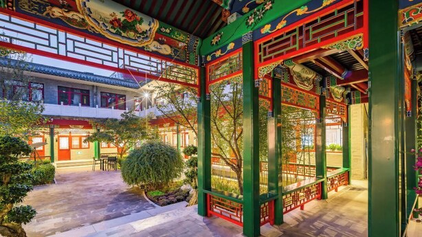 Une cour traditionnelle dotée d’une allée couverte, de plantes en pot et d’un bâtiment aux couleurs rouge et verte.