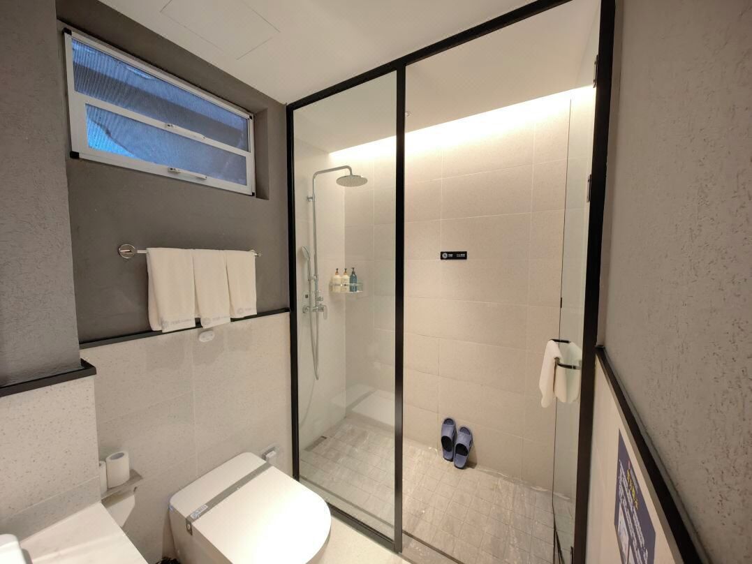 A modern bathroom with a glass shower enclosure, a toilet, a sink, and a towel rack.