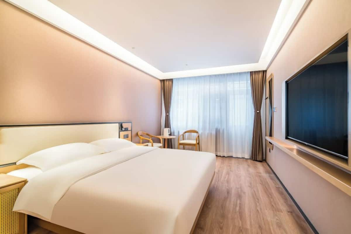 A hotel room with a large bed, a desk, a chair, and a TV.