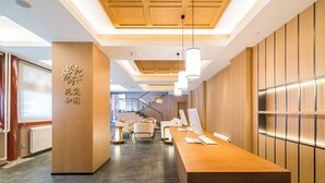 Un espace d’accueil moderne avec un comptoir de réception en bois, un coin salon avec des fauteuils et un escalier en arrière-plan.