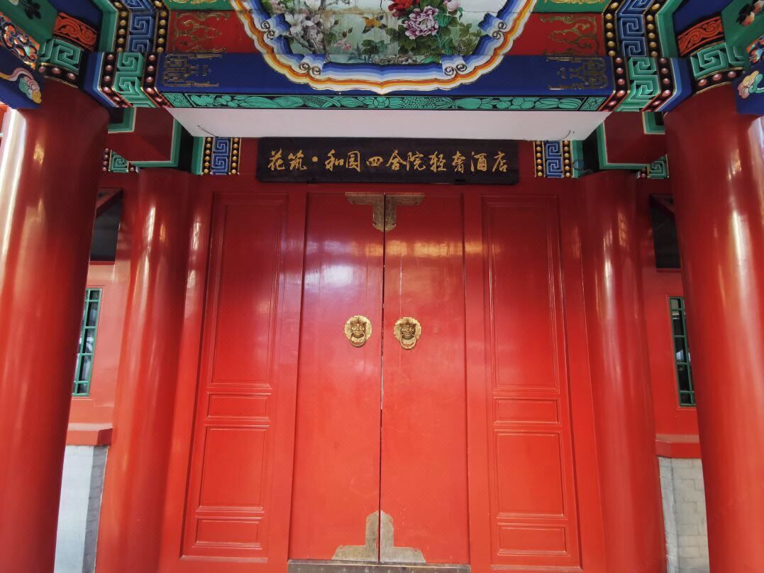 A red traditional Chinese gate with gold handles and a sign above it.