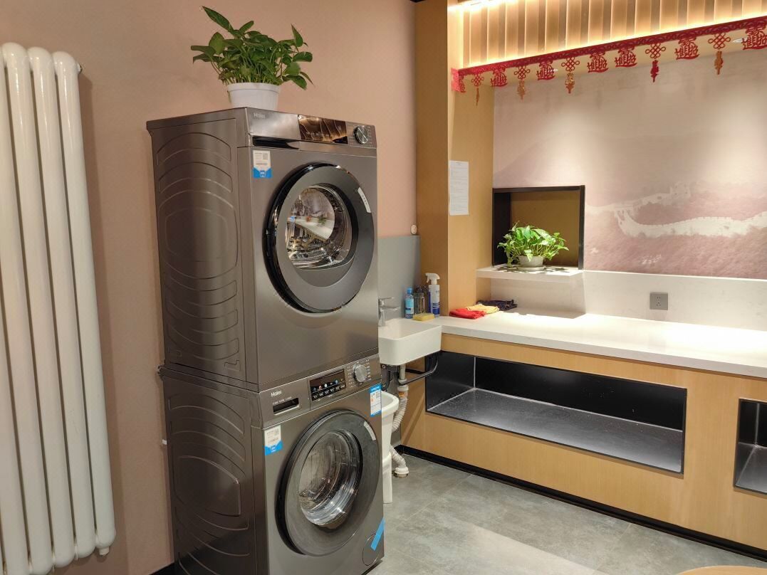 A compact laundry area with stacked washers and dryers, a sink, and a small countertop with a plant.