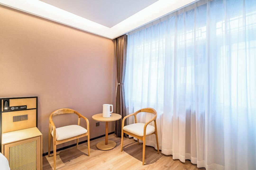 A hotel room with two wooden chairs, a small round table, a coffee maker, and a wall-mounted radio.