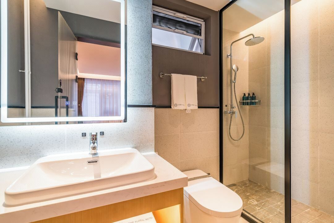 A modern bathroom with a large mirror, a sink, a toilet, and a glass-enclosed shower.